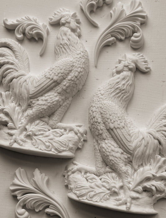 White clay castings of Iron Orchid Designs Chanticleer mould on a white background. two decorative roosters on floral plinths with swirls