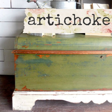 Vintage green trunk with 'artichoke' sign on a wooden floor.