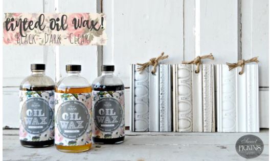 Three bottles of oil wax with labels on a wooden surface, accompanied by decorative trimmings in the background.