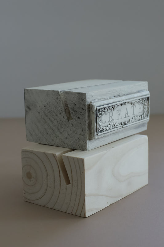 A small decorative wood stand with a distressed white painted top and a carved wood base, photographed against a plain gray background. From Iron Orchid Designs.