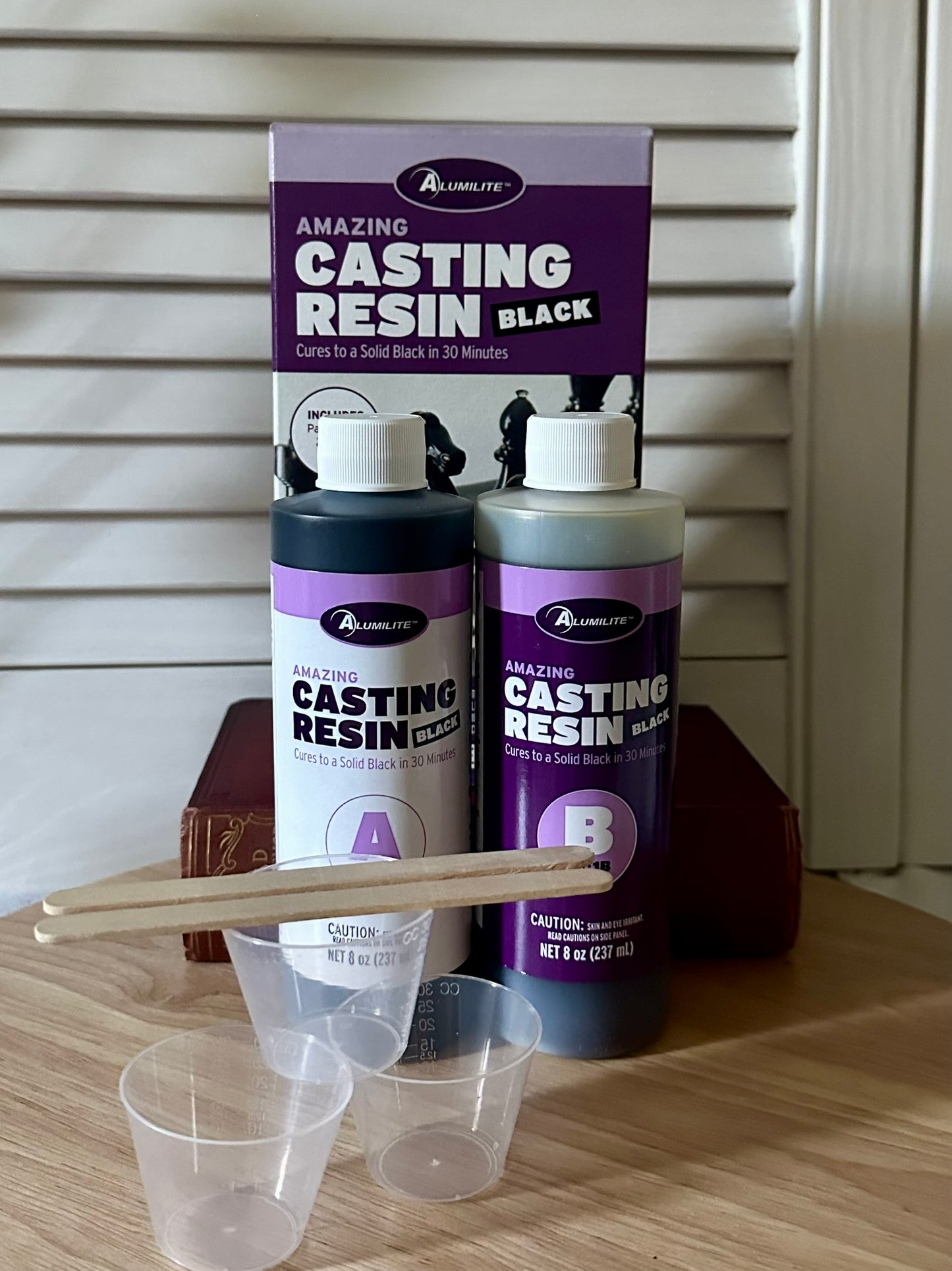 Alumilite Amazing Black Casting Resin set with bottles, a scoop, and a funnel on a wooden surface.