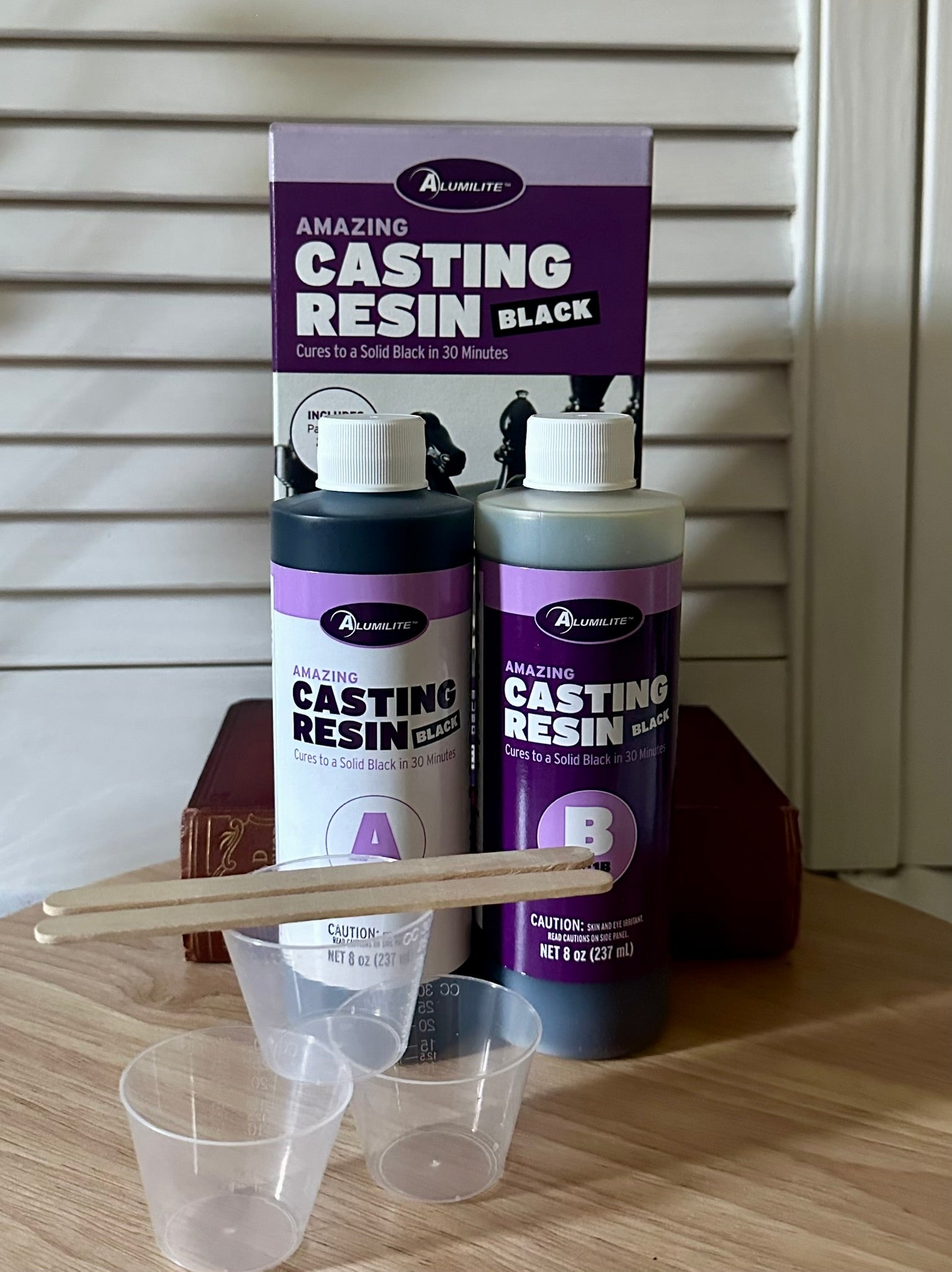Alumilite Amazing Black Casting Resin set with bottles, a scoop, and a funnel on a wooden surface.