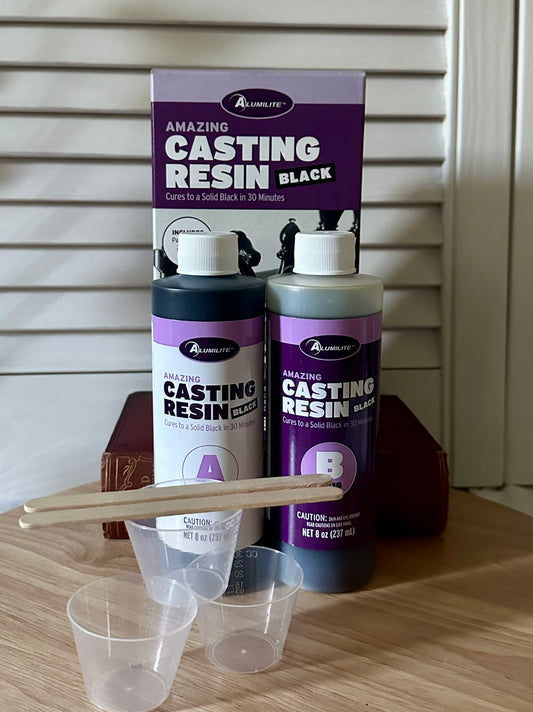 Alumilite Amazing Black Casting Resin set with bottles, a scoop, and a funnel on a wooden surface.