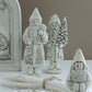 Three rustic white ceramic Santa Claus figurines with detailed carvings, displayed on a white surface with a neutral beige background. Belsnickel from Iron Orchid Designs.