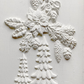 White embossed holiday wall decor featuring a poinsettia, holly, pinecones, and snowflake designs on a textured white background. Boughs of Holly Iron Orchid Designs