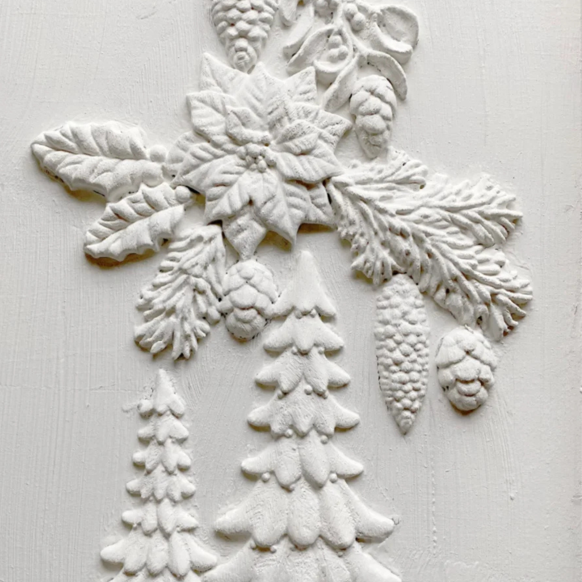 White embossed holiday wall decor featuring a poinsettia, holly, pinecones, and snowflake designs on a textured white background. Boughs of Holly Iron Orchid Designs