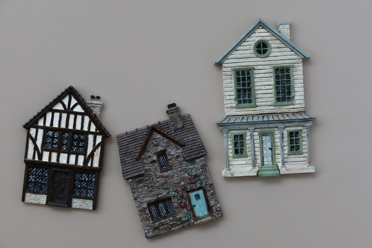 Three miniature decorative house figurines in different architectural styles displayed on a plain beige background. Charlbury Lane From Iron Orchid Designs.