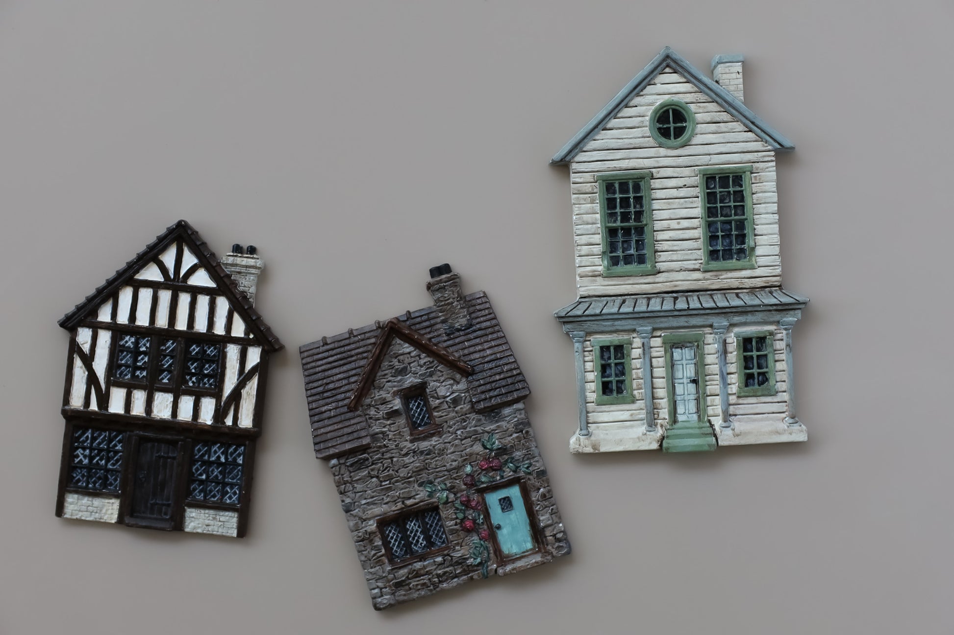 Three miniature decorative house figurines in different architectural styles displayed on a plain beige background. Charlbury Lane From Iron Orchid Designs.