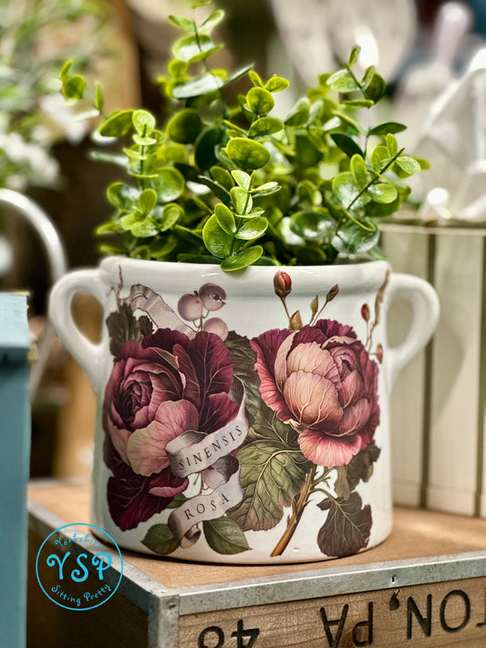 Decorative white ceramic flower pot with floral design on a wooden surface