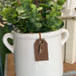 Reverse side of a white ceramic flower pot with green plant and brown tag and key on a wooden surface