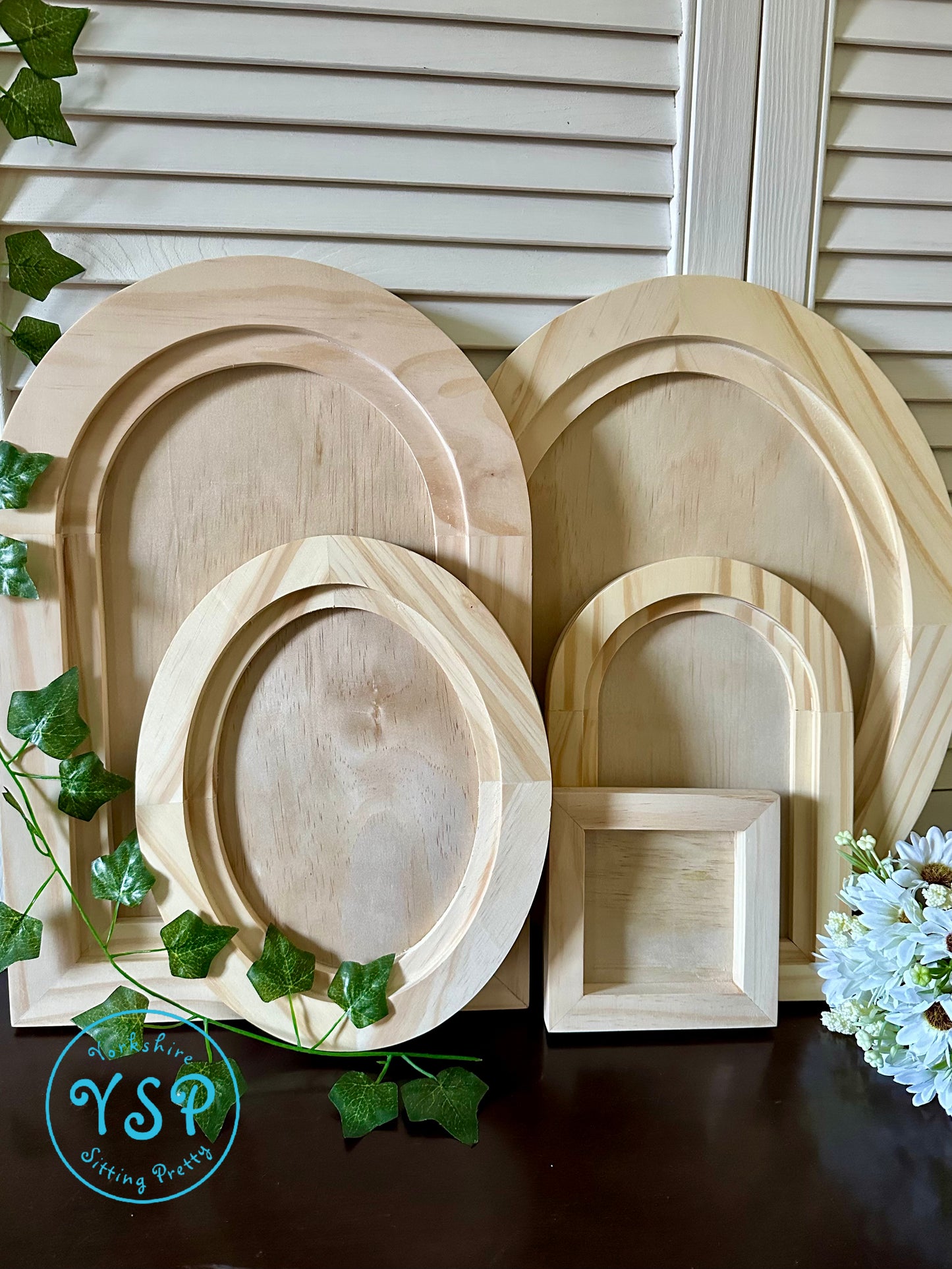Set of wooden frames of different shapes and sizes on a dark surface with greenery by Iron Orchid Designs