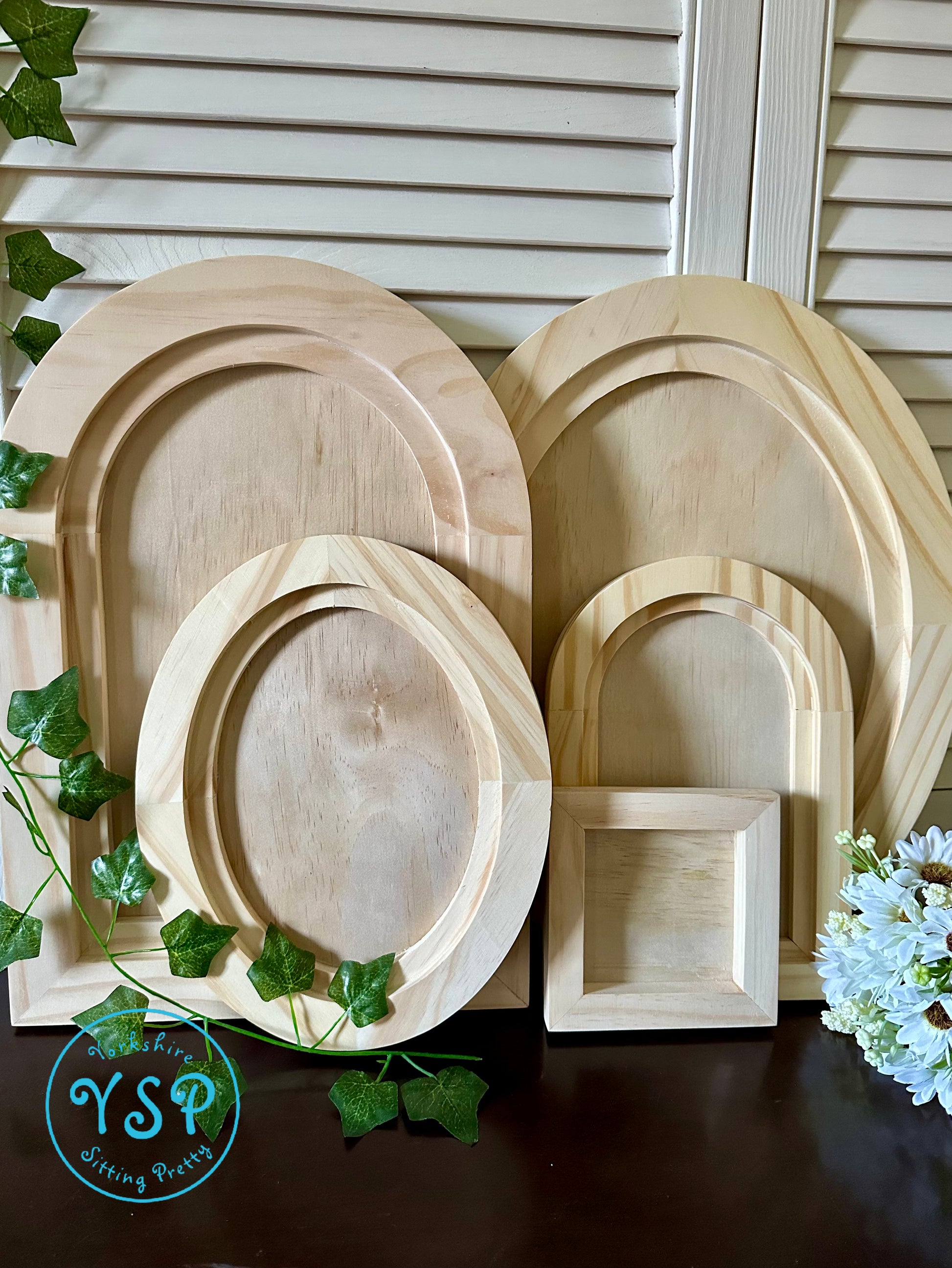 Set of wooden frames of different shapes and sizes on a dark surface with greenery by Iron Orchid Designs