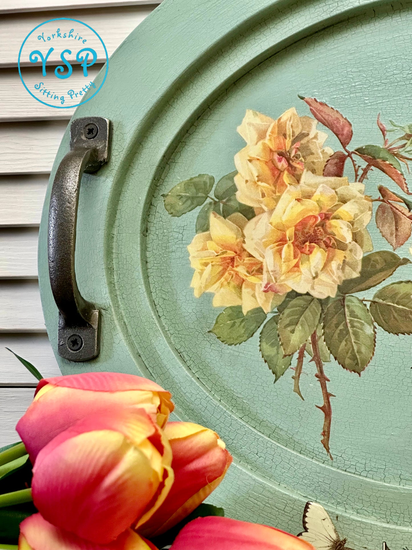 Oval green tray with floral design and pink tulips in the foreground