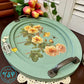 Decorative oval tray with floral design and vintage-style handles on a table.