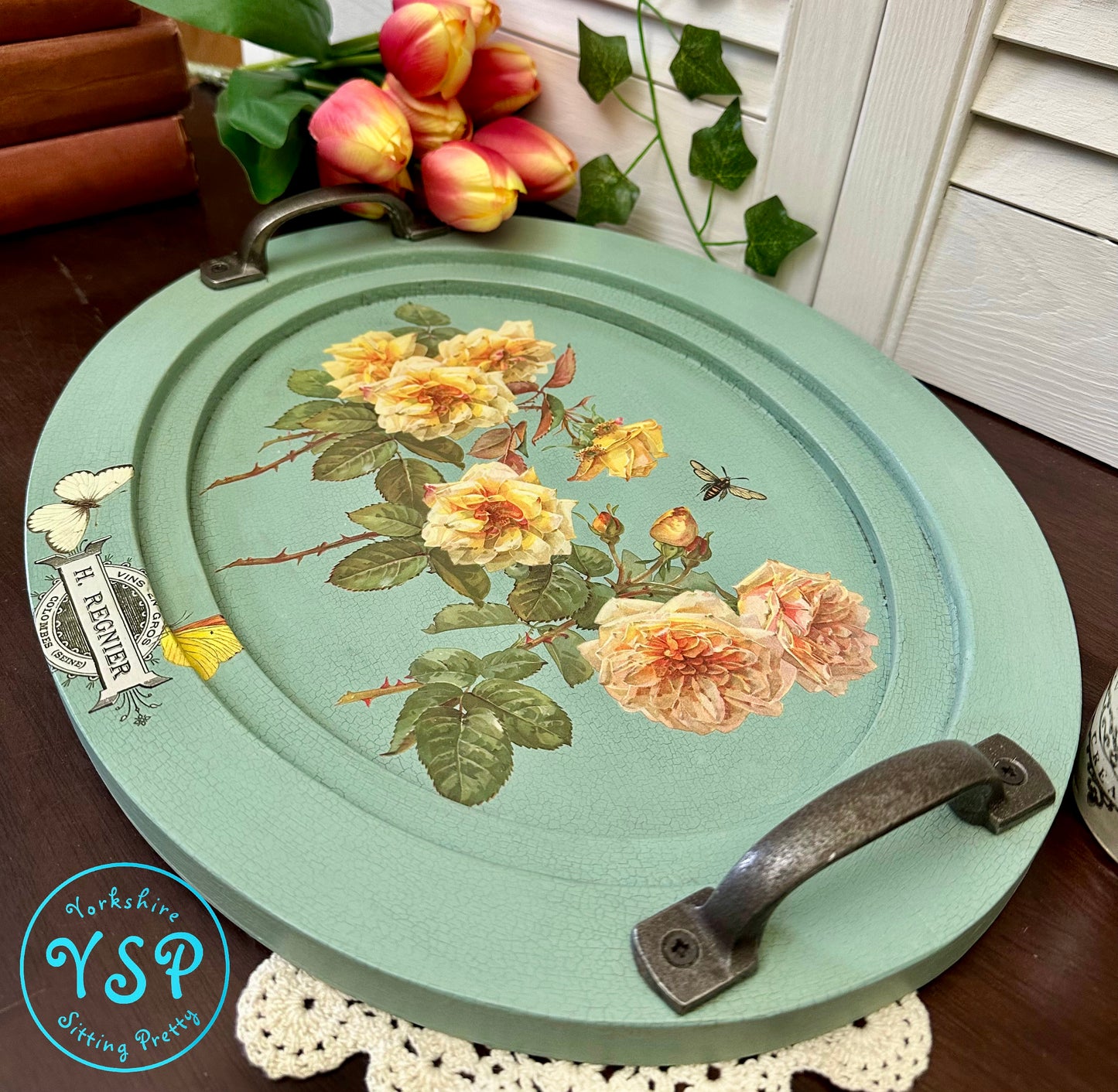 Decorative oval tray with floral design and vintage-style handles on a table.