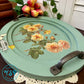 Oval decorative tray with floral design on a table with flowers in the background