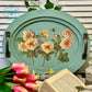 Decorative oval tray with floral design on a table with tulips and a book.