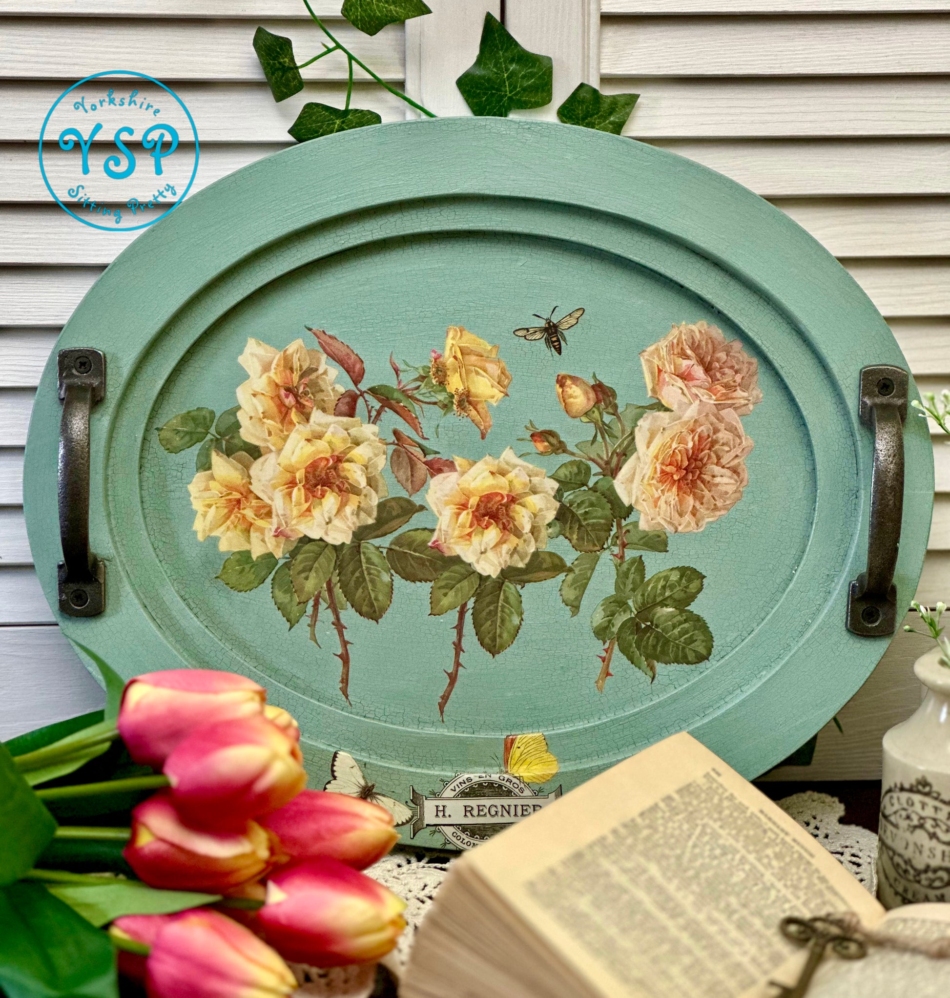 Decorative oval tray with floral design on a table with tulips and a book.