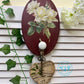Decorative wall hook with floral design and music sheet heart, on a white wooden background.