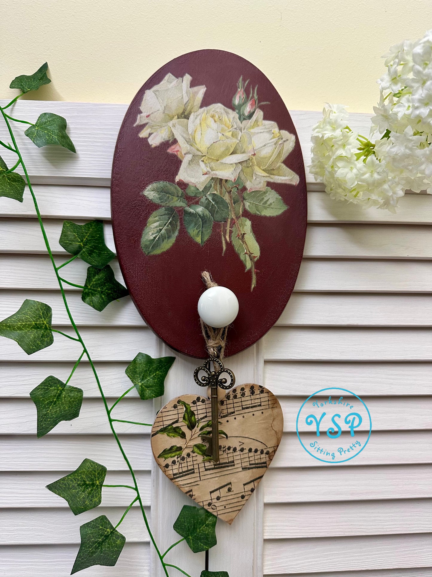 Decorative wall hook with floral design and music sheet heart, on a white wooden background.