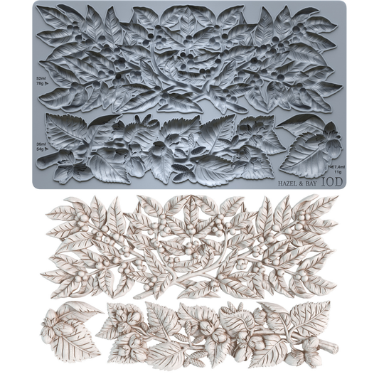 A gray silicone baking or craft mold sheet with embossed floral and leaf patterns, shown above a set of matching light beige carved floral and leaf pieces on a white background. Hazel and Bay. From Iron Orchid Designs.