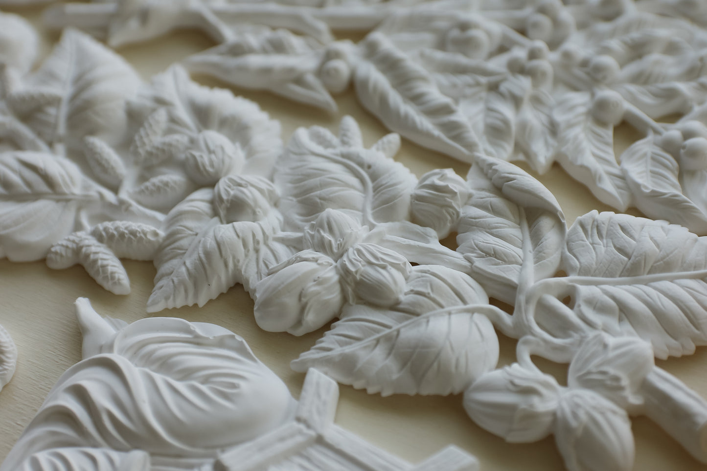 White clay floral and leaf relief sculpture on a light beige background. Hazel and Bay mould. From Iron Orchid Designs.
