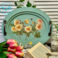 Decorative tray with floral design on a wooden surface with flowers and an open book.