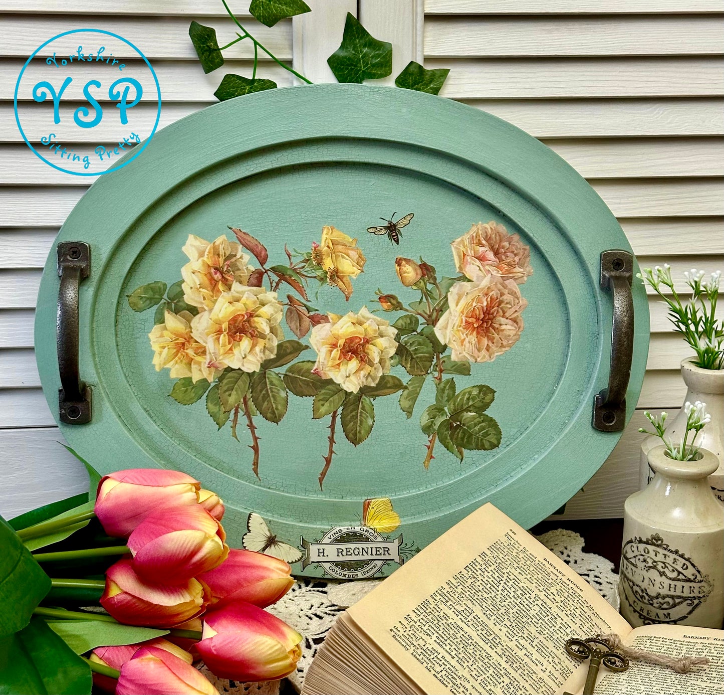 Decorative tray with floral design on a wooden surface with flowers and an open book.