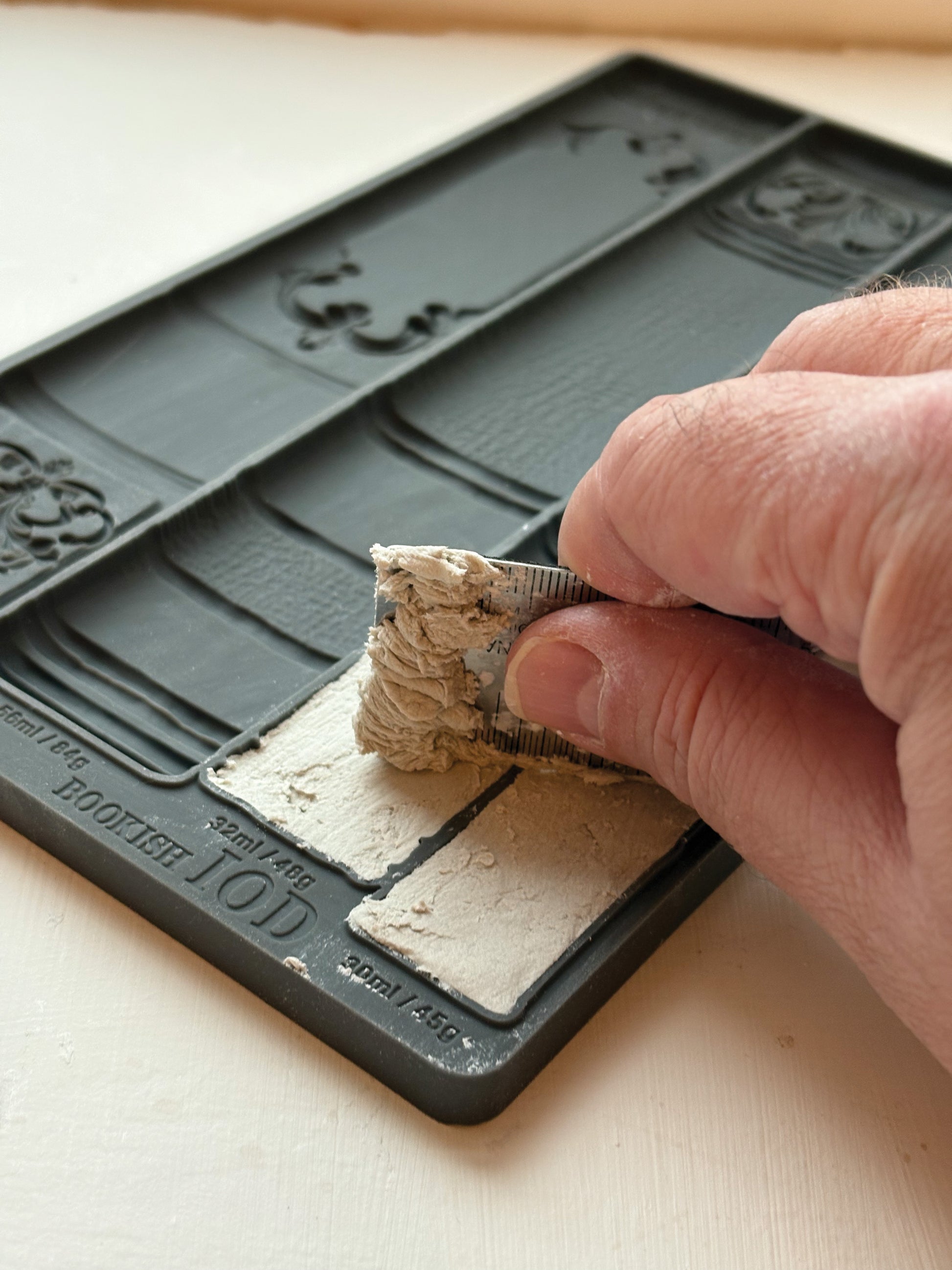 Hand using a tool to shape a small block of material on a decorative mould from Iron Orchid Designs Bookish mould