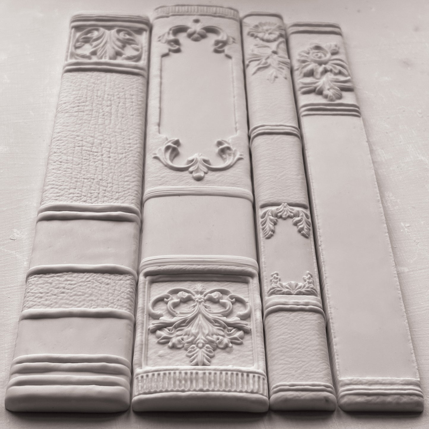 Decorative white bookends with intricate designs on a grey surface from Iron Orchid Designs Bookish mould