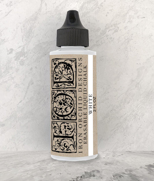 A bottle of Iron Orchid Designs erasable liquid chalk in white, with a decorative label featuring intricate patterns.