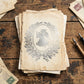 A stack of vintage aged paper letters with a central illustration of an angel, displayed on a rustic wooden table alongside old stamps and two fountain pens. From Iron Orchid Designs