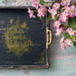 Decorative black and gold tray with floral design and pink flowers on a rustic wooden surface