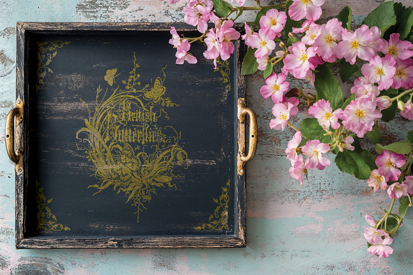 Decorative black and gold tray with floral design and pink flowers on a rustic wooden surface