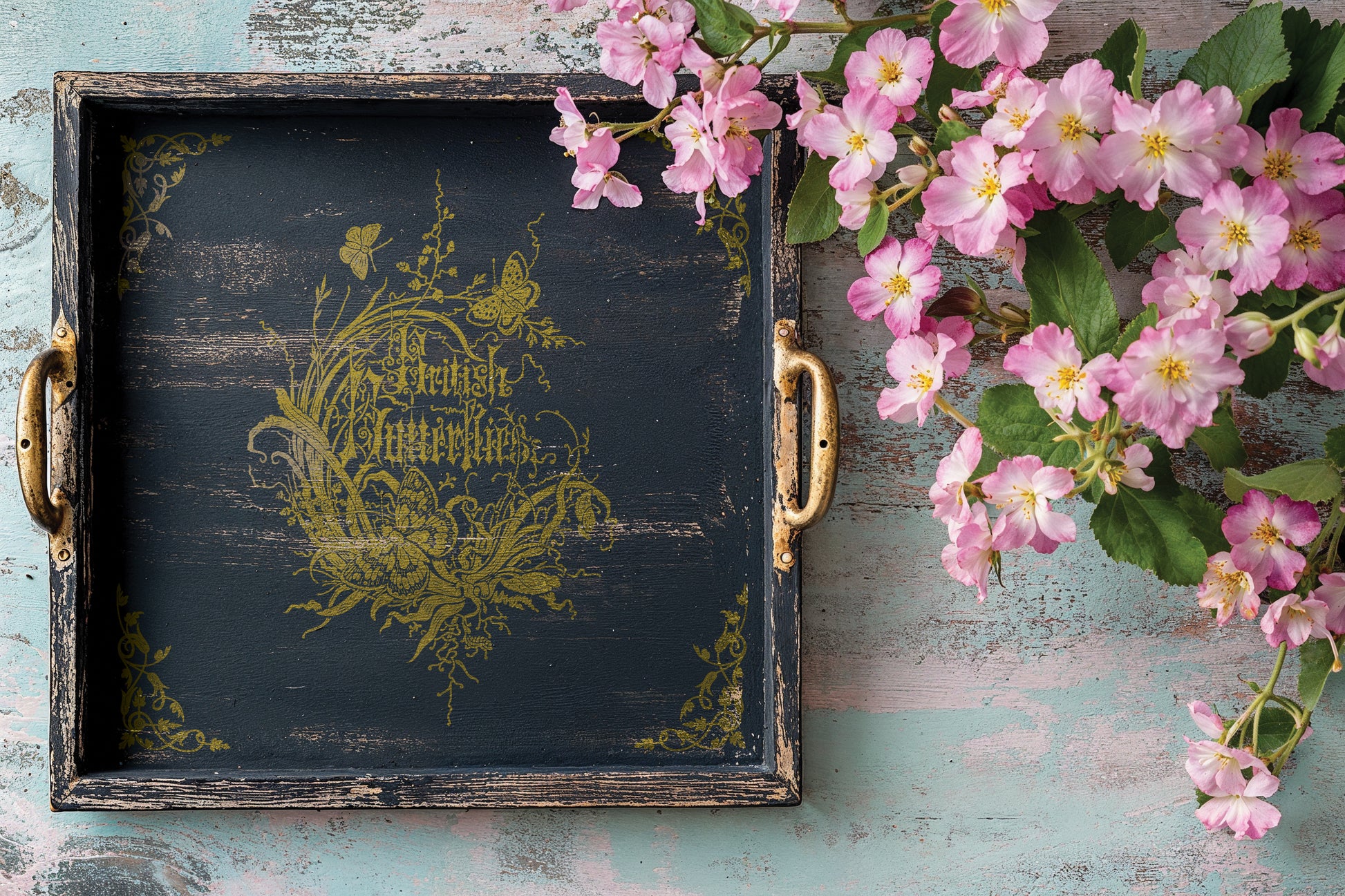 Decorative black and gold tray with floral design and pink flowers on a rustic wooden surface