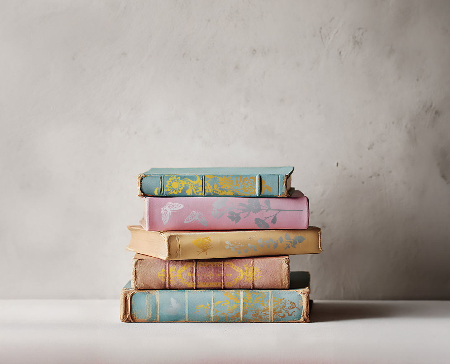 Stack of colourful books with decorative covers on a neutral background. The books have decorative spines created by Iron Orchid Designs Papillon transfer