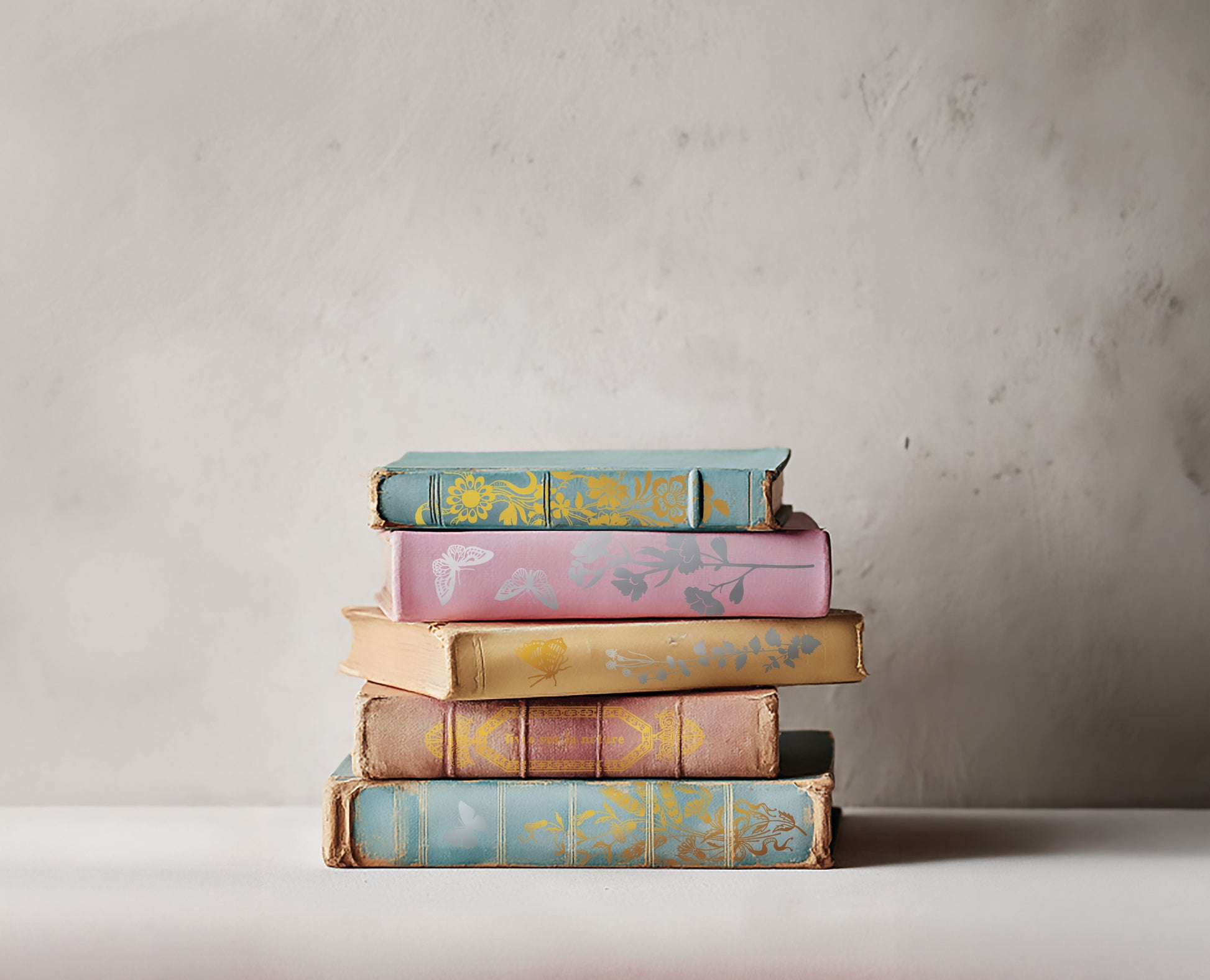 Stack of colourful books with decorative covers on a neutral background. The books have decorative spines created by Iron Orchid Designs Papillon transfer