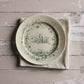 Decorative plate with bird and floral design in green on a textured surface