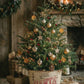 A decorated Christmas tree in a vintage Santa-themed bucket, styled in a cozy rustic living room with a stone fireplace, candles, wrapped gifts, and pinecones. From Iron Orchid Designs