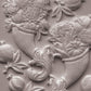 White clay decorative wall relief featuring pomegranate motifs and floral baskets on a textured light gray surface. Cornucopias mould. From Iron Orchid Designs.