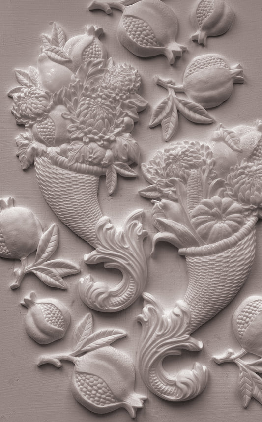 White clay decorative wall relief featuring pomegranate motifs and floral baskets on a textured light gray surface. Cornucopias mould. From Iron Orchid Designs.