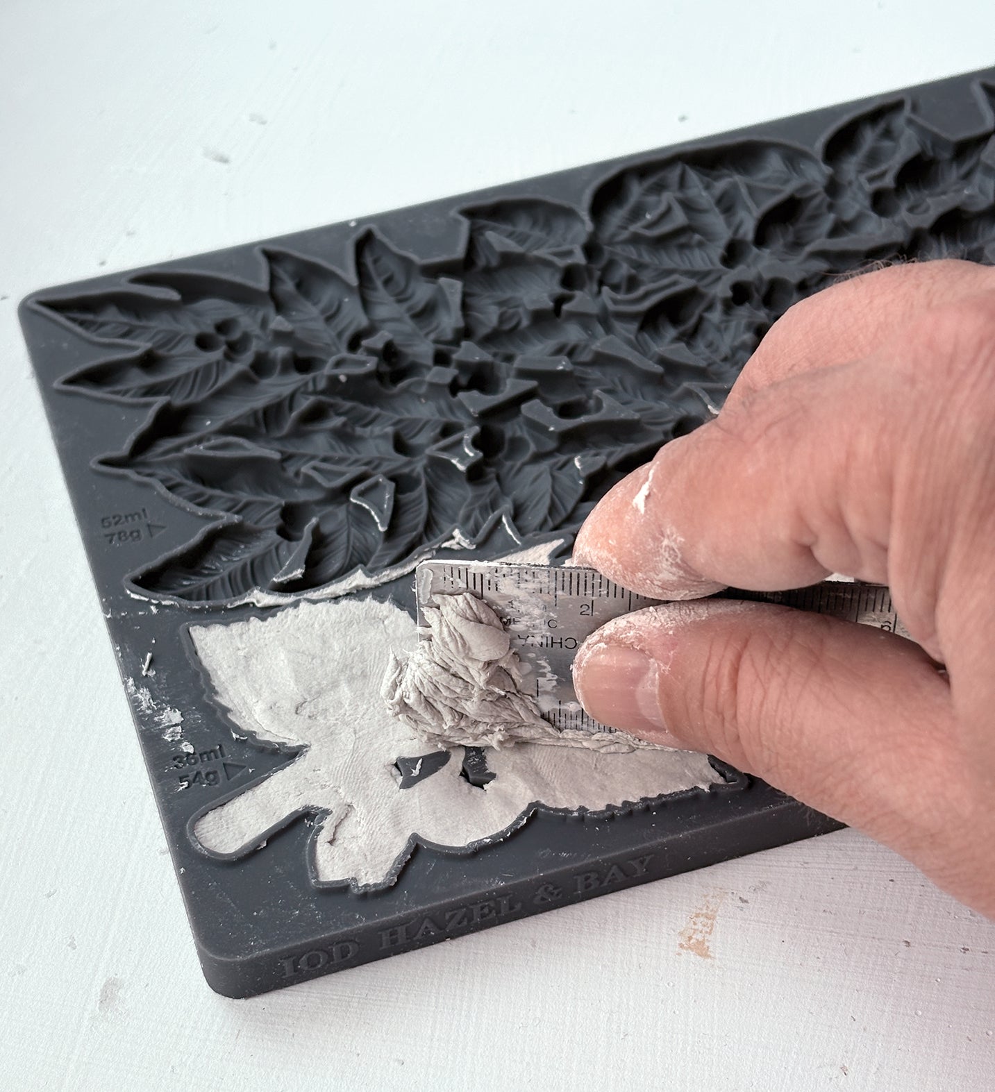 A close-up of a hand pressing a gray stamping ink pad into a grey floral silicone mold, with the embossed design becoming visible on the surface From Iron Orchid Designs.. 