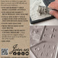 Back cover of the Iron Orchid Designs 'With the Iod Family' Iod Moulds book, featuring product information, website details, and a photo of a hand holding a cast replica of the Iod Orchid flower. From Iron Orchid Designs.