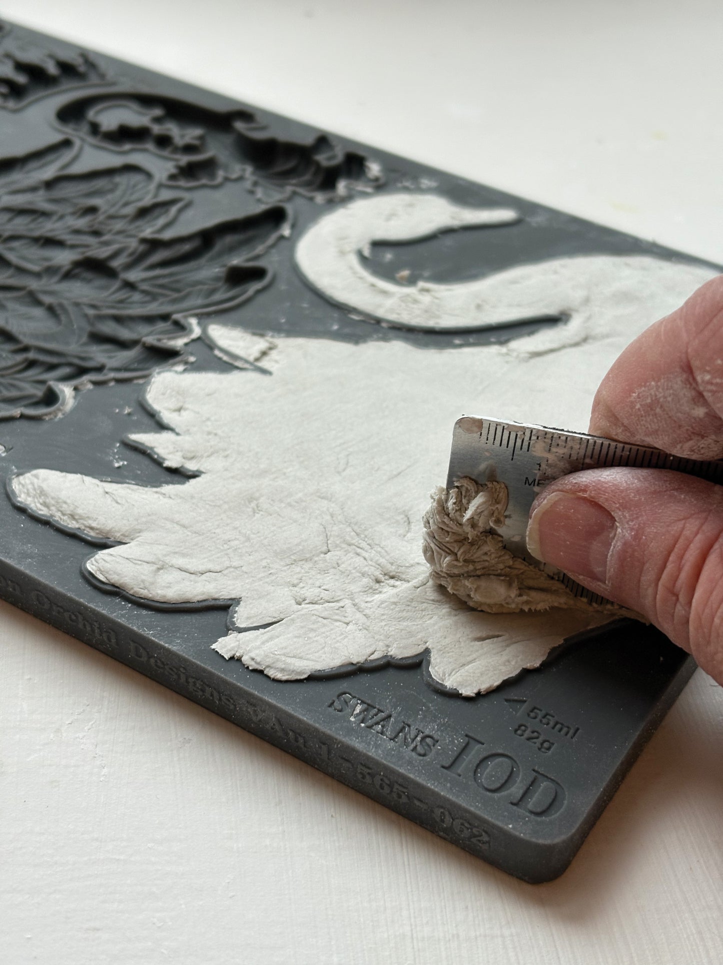 Hand using a metal ruler to fill a silicone mould with air dry clay. Taken  from Iron Orchid Designs Swans Mould