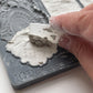 A close up image of a hand scraping away excess clay from Iron Orchid Designs Conservatory Labels mould