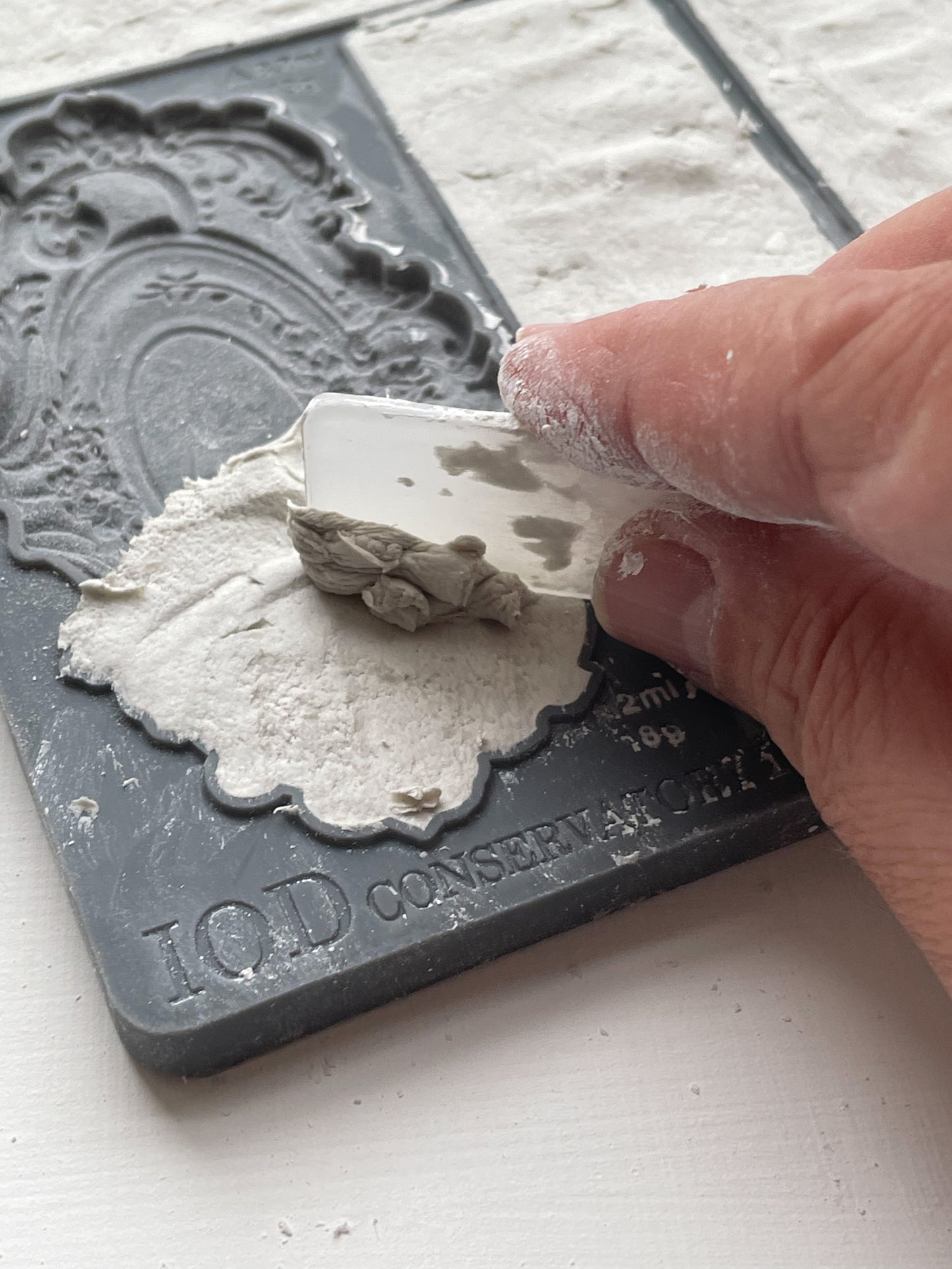 A close up image of a hand scraping away excess clay from Iron Orchid Designs Conservatory Labels mould