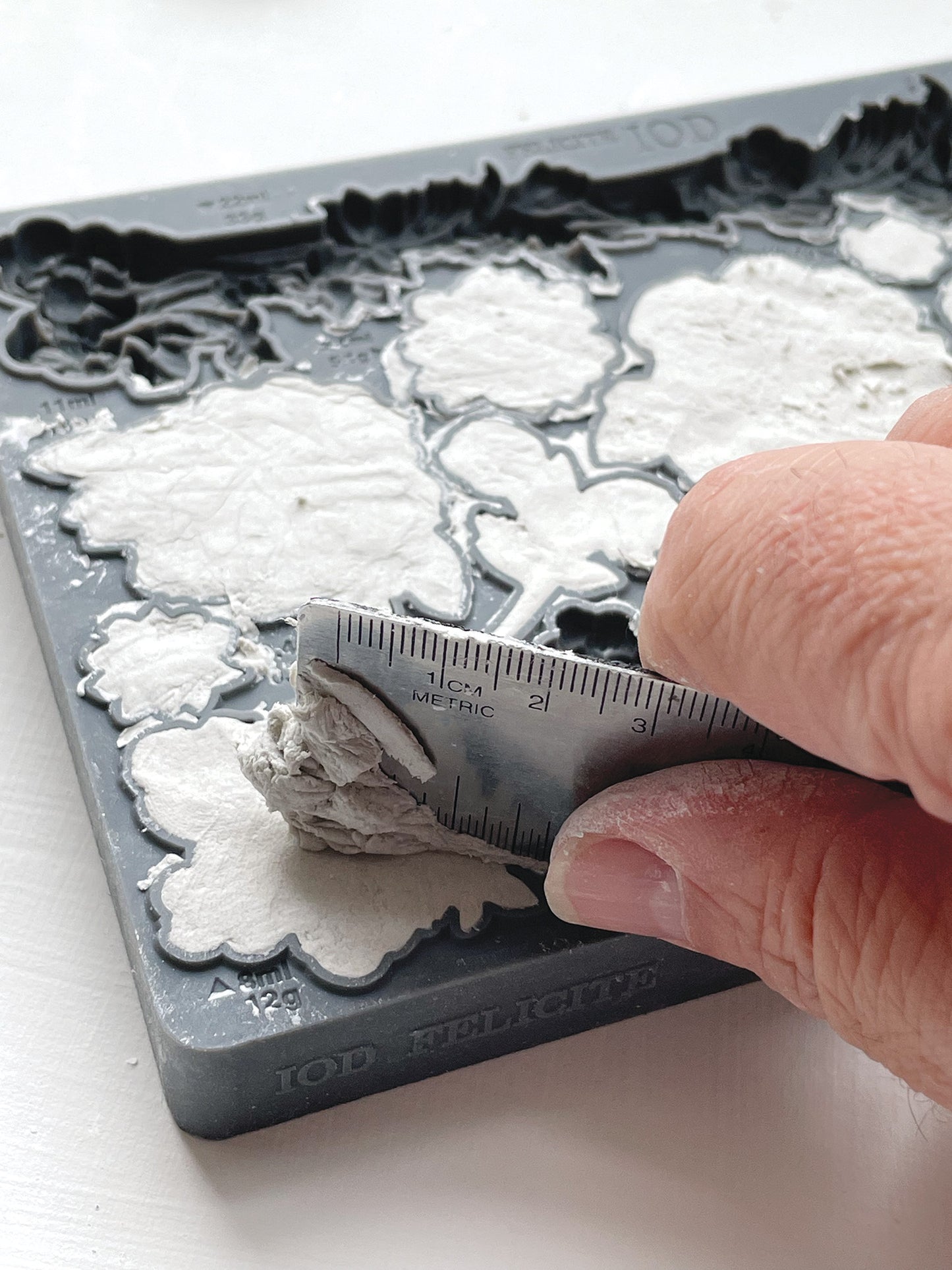 A close up image of a hand scraping excess clay using a metal ruler from Iron Orchid Designs Felicite mould