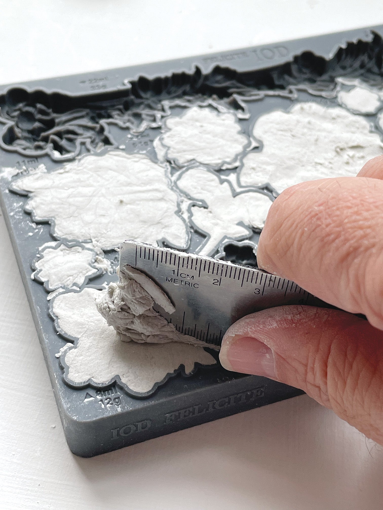 A close up image of a hand scraping excess clay using a metal ruler from Iron Orchid Designs Felicite mould