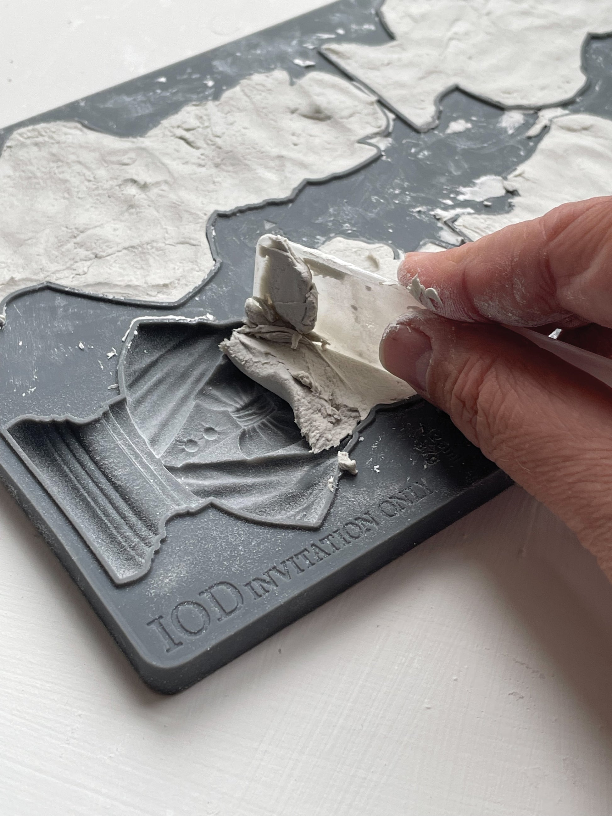A close  up image of a hand removing excess clay from Iron Orchid Designs Invitation Only mould