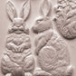 Close up of white castings from iron Orchid Designs Les Lapins mould. Three white clay rabbits, a basket and an egg on a white background.